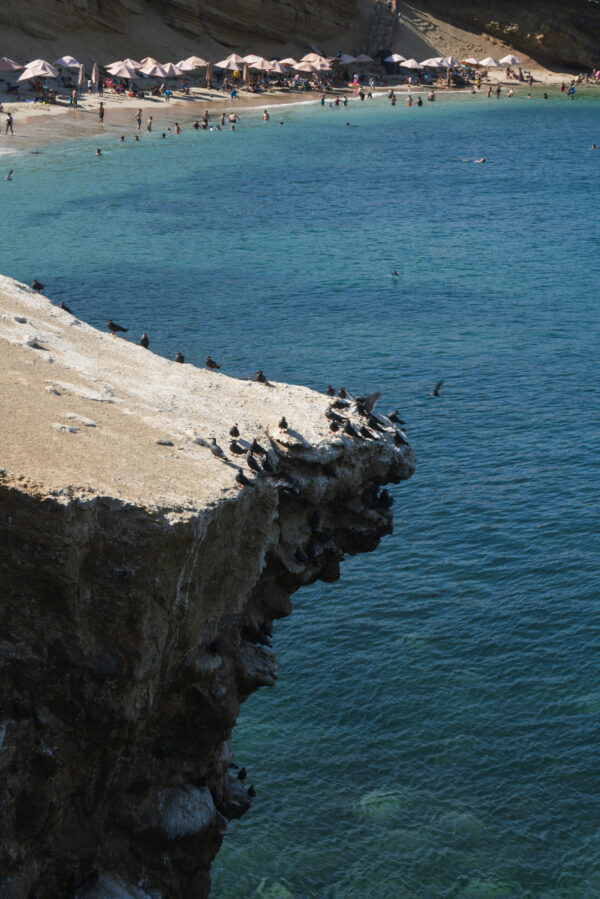 Playa Raspon Paracas - Vista de la hermosa Playa Raspon con sus sombrillas y turistas disfrutando de sus aguas cristalinas, ubicada en la región de Paracas Ica.