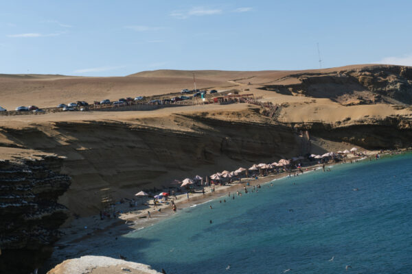 Playa Raspon Paracas - Vista de la hermosa Playa Raspon con sus sombrillas y turistas disfrutando de sus aguas cristalinas, ubicada en la región de Paracas Ica.